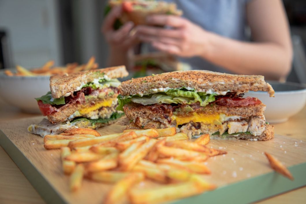 Club Sandwich mit Pommes mit Person im Hintergrund beim Essen