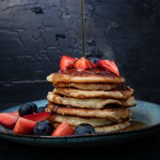 fluffige american pancakes gestapelt mit erbeeren, blaubeeren und Ahornsirup vor dunkeln Hintergrund