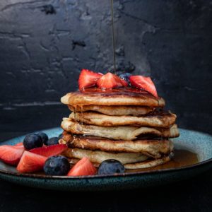american pancakes stapel vor dunklen hintergrund mit erbeeren, blaubeeren und ahornsirup