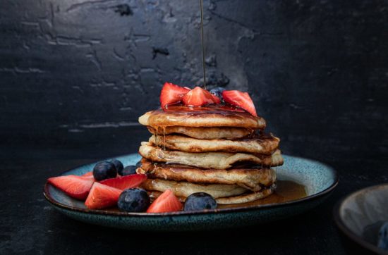 american pancakes stapel vor dunklen hintergrund mit erbeeren, blaubeeren und ahornsirup