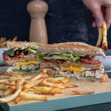 club sandwich aufgeschnitten auf einem Brett mit Pommes und Ketchup im Hintergrund